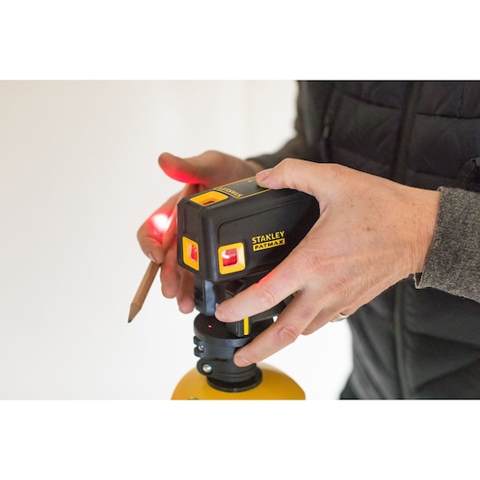 Photo of STANLEY FMHT1-77413 laser level in use, hand adjusting device, yellow and black housing.