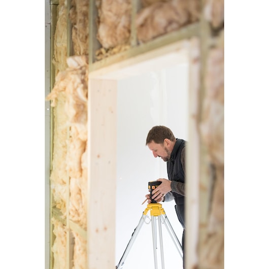 STANLEY FMHT1-77413 laser level on tripod used during construction, side angle, insulation visible on wall.