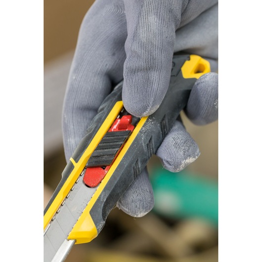 Photo of STANLEY FMHT10338-0 utility knife close-up, black and yellow handle, being held with gloved hand.