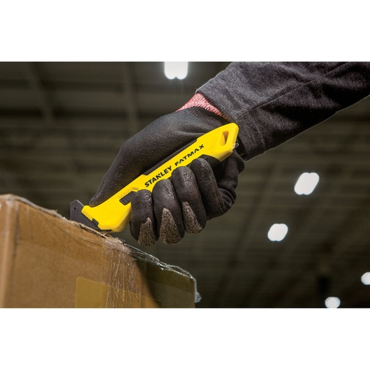 STANLEY FMHT10358-0 utility knife with yellow handle cutting box, shown held in gloved hand.