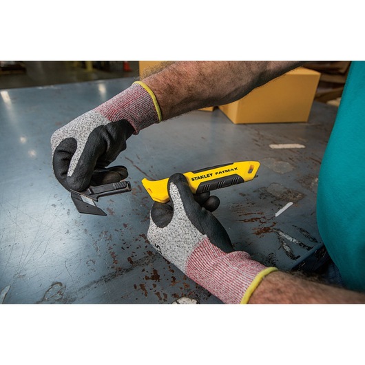 Photo of STANLEY FMHT10358-0 utility knife with yellow handle being held by gloved hands on a metal table.