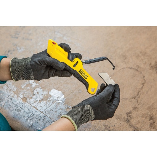 Photo of STANLEY FMHT10365-0 utility knife with yellow handle and blade being replaced by gloved hands.