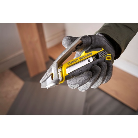 Photo of STANLEY FMHT10594-0 utility knife, yellow and black, held in gloved hand during cutting task.