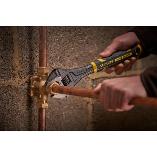 STANLEY FMHT13125-0 adjustable wrench in use on copper plumbing, close-up photo.