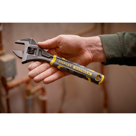 STANLEY FMHT13126-0 adjustable wrench with yellow and black handle, held in hand, shown in workshop setting.