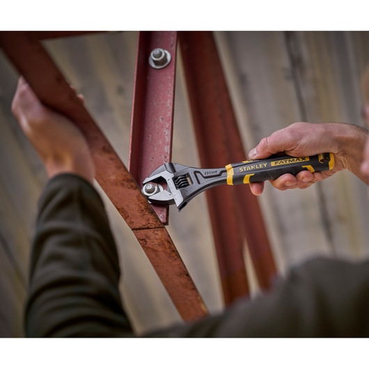 Stanley FMHT13127-0 adjustable wrench used to tighten bolt on red metal beam, close-up action shot.