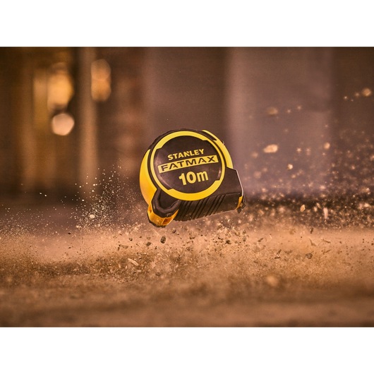 STANLEY FMHT33005-0 10m FATMAX tape measure in yellow and black, shown mid-air in dusty environment.