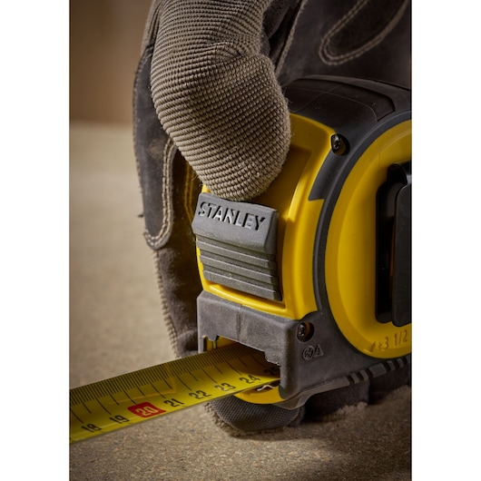 Stanley FMHT33005 tape measure held by gloved hand, close-up side view on flat surface.
