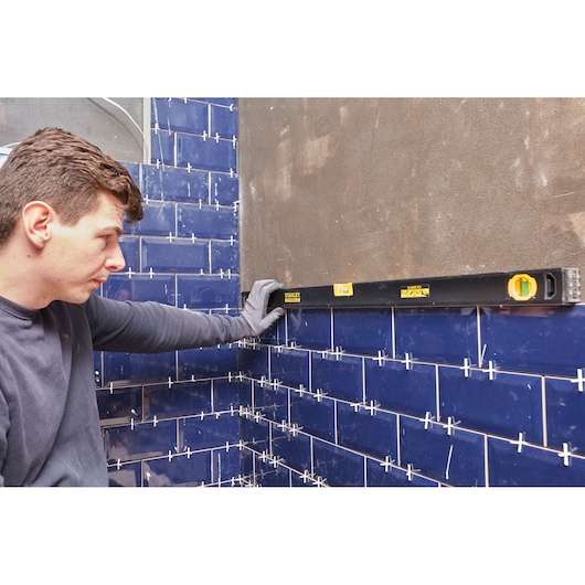 STANLEY FMHT42447-1 spirit level held against blue tiled wall; construction context.