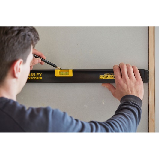 Photo of STANLEY FMHT42554-1 spirit level in use on a wall, person marking line with pencil.