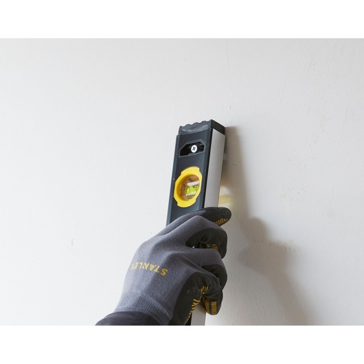Photo of STANLEY FMHT42561-1 spirit level held vertically against a wall by a gloved hand.