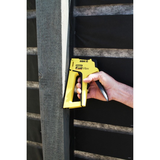 STANLEY FMHT6-70411 hand stapler, yellow, shown in use against a wooden beam.
