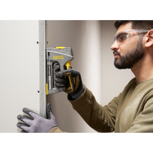 STANLEY FMHT6-70868 stapler used on drywall, close-up of worker's gloved hand in action.