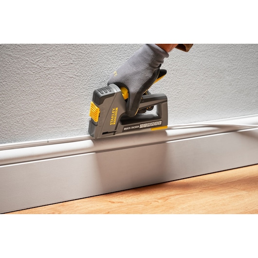 Photo of STANLEY FMHT6-70868 multi-tacker in use attaching trim to wall, held by gloved hand.
