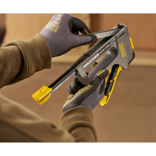 Stanley FMHT6-70868 multi-tacker being loaded with staples by gloved hands in workshop setting.
