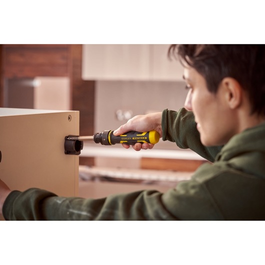 Stanley FMHT62692-0 screwdriver in use to assemble furniture, yellow and black handle, indoor setting.