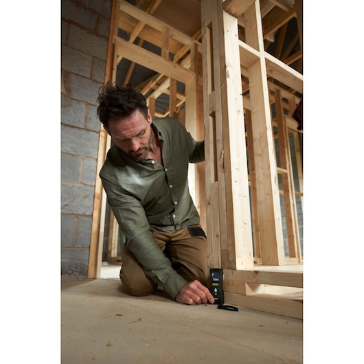STANLEY FMHT77165-0 laser distance measurer in use at construction site, angled front view.