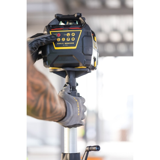 Photo of STANLEY FMHT77447-1 rotary laser level operated by a gloved hand, product in use outdoors.