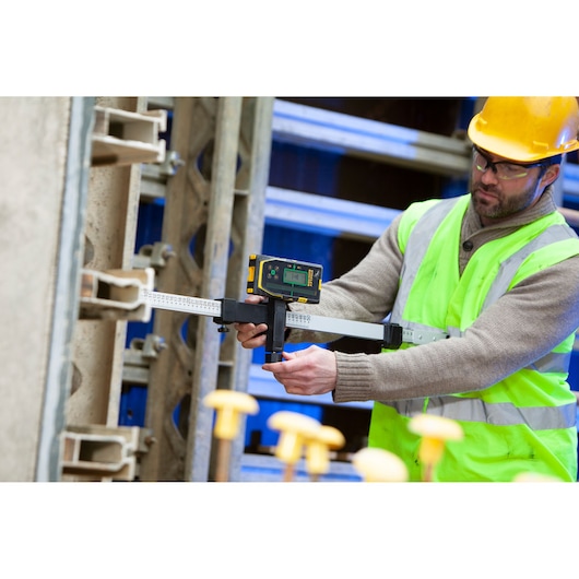 STANLEY FMHT77653-0 digital measuring tool in use on construction site, held by worker in safety gear.