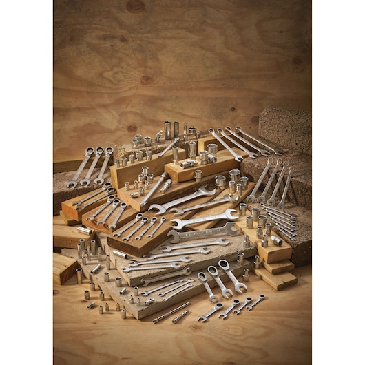 Assorted wrenches and socket tools arranged on wooden blocks and concrete against a wooden background.