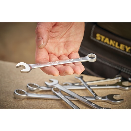 Stanley FMMT13041-0 combination wrench held in hand, with more wrenches on a table, tool belt visible.