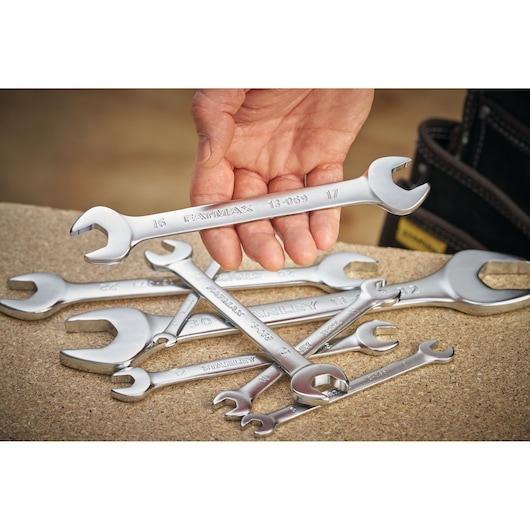 Stanley FMMT13062-0 photography of hand holding chrome open-end wrench with other wrenches on workbench.
