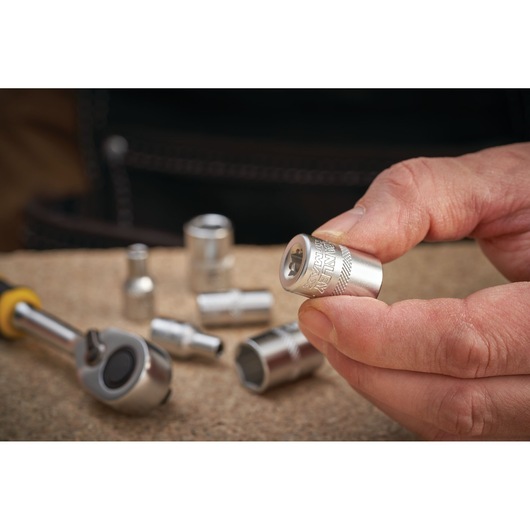 Photo of a hand holding a STANLEY socket, SKU FMMT17197-0, with ratchet and sockets on a work surface.