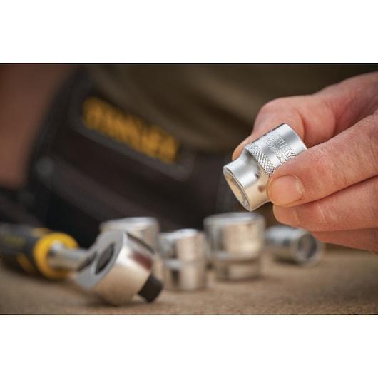 Photo of STANLEY FMMT17212-0 socket set, close-up of hand holding a silver socket with ratchet tool in background.