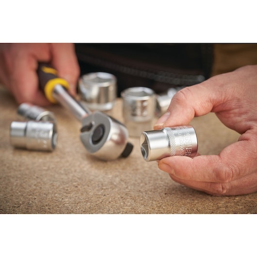 STANLEY FMMT17246-0 socket set photography with hand holding a chrome socket and ratchet tool on a work surface.