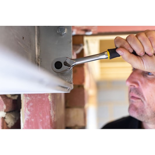 STANLEY FMMT82826-1 ratchet wrench in use tightening bolt near metal and brick wall, side angle.