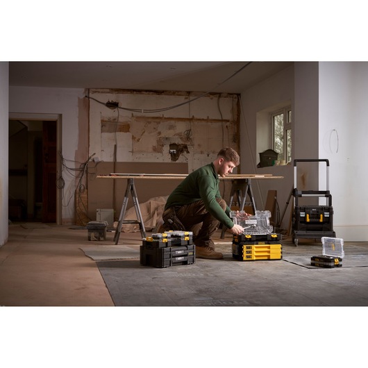 Person organizing STANLEY storage cases and tools in a room under renovation. Cases are stacked on the floor.