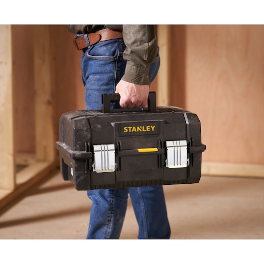 Stanley FMST1-71219 toolbox with metal latches and handle, carried by person in workshop setting.