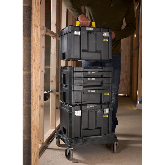 STANLEY FMST1-71972 stackable black toolboxes on rolling cart in workshop, person lifting top box.