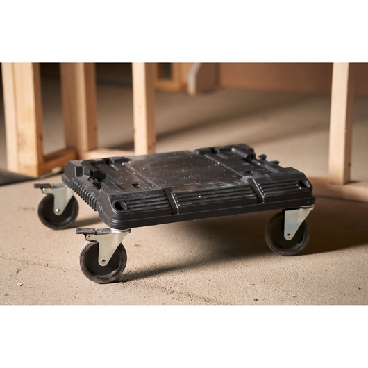 STANLEY FMST1-71972 black plastic rolling dolly with four swivel casters, shown on a workshop floor.