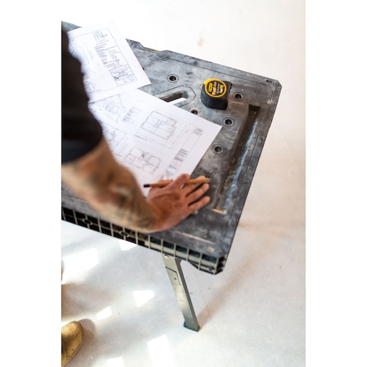 Photo of STANLEY FMST1-75672 work table with building plans and tape measure on top, angled from above.