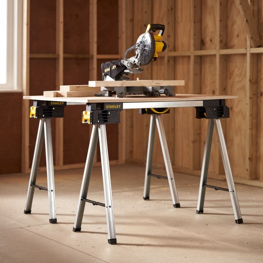 Photo of STANLEY FMST1-75763 work stand with miter saw and wood boards, shown in workshop setting.