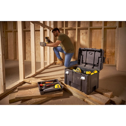 Photo of STANLEY FMST1-75796 tool box with open lid, tools inside, placed on wooden planks at a construction site.