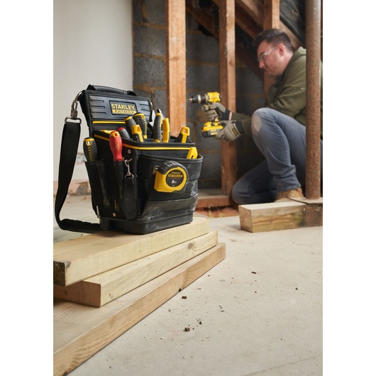 STANLEY FMST17624-1 tool bag filled with hand tools, tape measure, and drill, shown at a construction site.