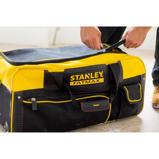 STANLEY FMST82706-1 large yellow and black soft tool bag with zipper, being opened by hand.