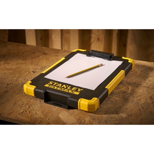 STANLEY FMST82721-1 clipboard with yellow corners, pencil and paper, angled view on wooden table.
