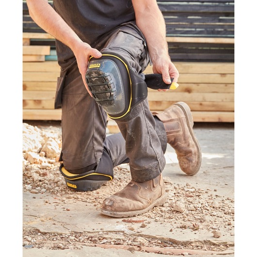 STANLEY FMST82960-1 knee pad with black and yellow trim being strapped on by worker outdoors.
