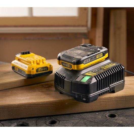 Photo of STANLEY SFMCB12D2 yellow 20V battery and charger set on wooden planks in workshop.