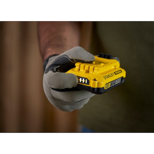 Photo of STANLEY SFMCB12D2 yellow V20 battery held in gloved hand, product photography close-up.