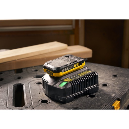 STANLEY SFMCB202 battery and charger with yellow accents on workshop table, front angle.