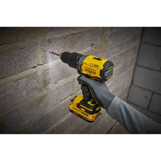 STANLEY SFMCD715D2K cordless drill in use drilling into a brick wall, shown in a close-up side angle.