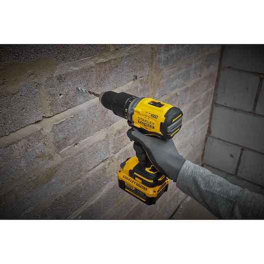 STANLEY SFMCD715M2K cordless drill in use drilling into a brick wall, bright yellow and black design.
