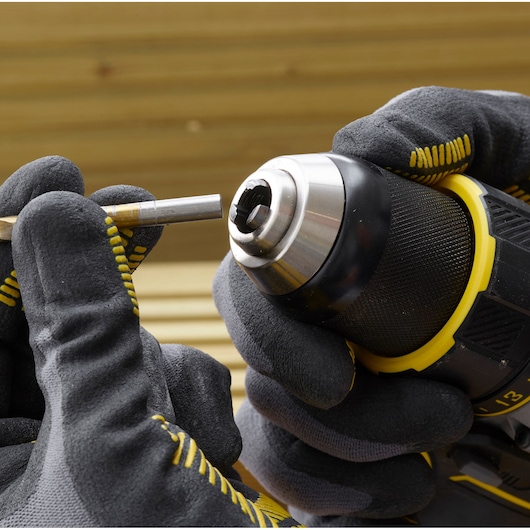 Stanley SFMCD720B drill close-up with gloved hands holding a metal drill bit, photography product image.