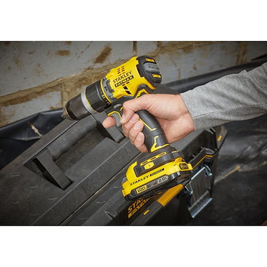 Photo of STANLEY SFMCD721D2K yellow cordless drill held by hand near black toolbox.