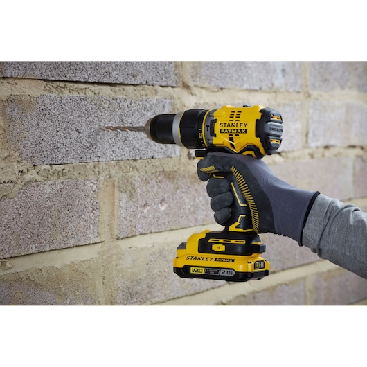 Photo of STANLEY SFMCD721D2K cordless drill in use on brick wall, yellow and black design, side angle.