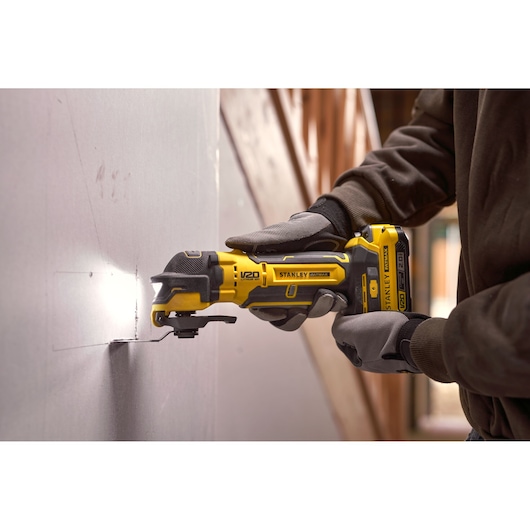 Stanley SFMCE510B oscillating tool cutting drywall, close-up in use with gloved hands.